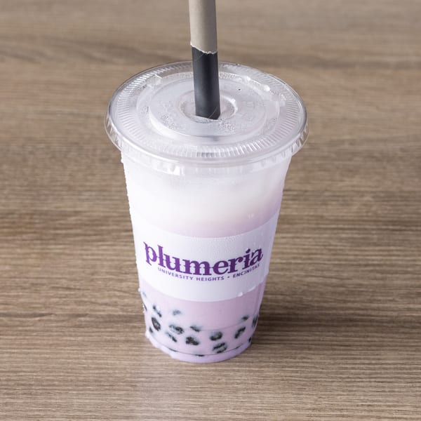 Plumeria taro bubble tea with tapioca pearls and a straw on a wooden table.