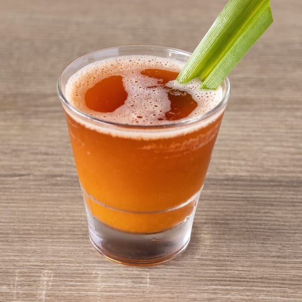 A vibrant orange drink with a foamy top, garnished with a green leaf, on a wooden table.
