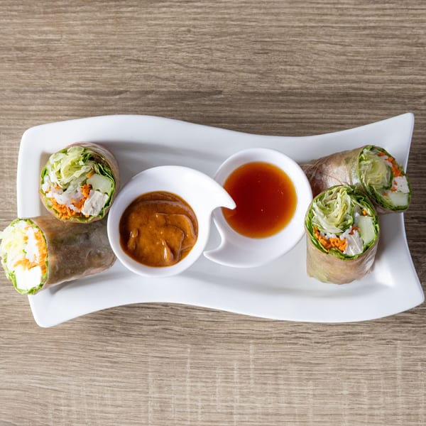 Four fresh spring rolls with chicken, vegetables, and rice noodles, served with peanut and sweet chili sauces.