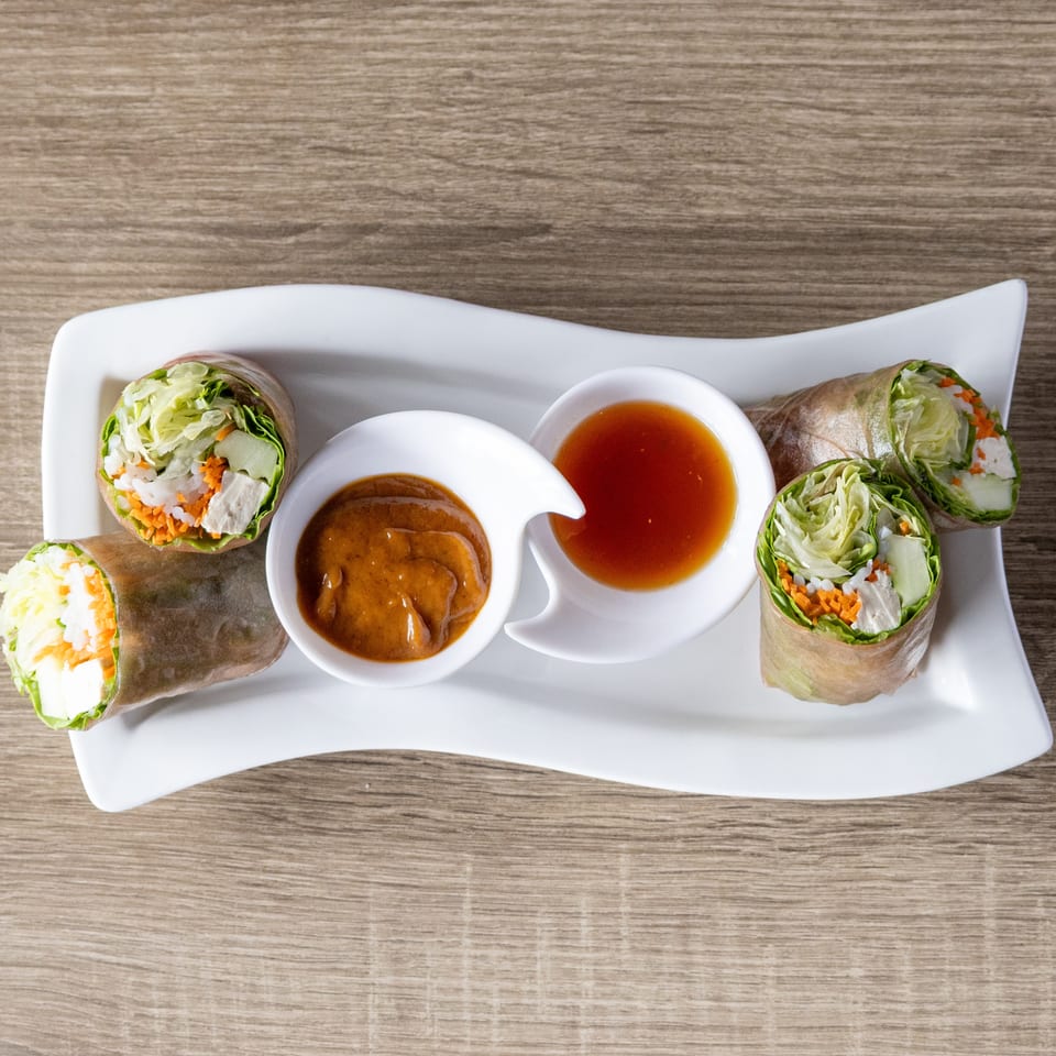 Four fresh spring rolls with chicken, vegetables, and rice noodles, served with peanut and sweet chili sauces.