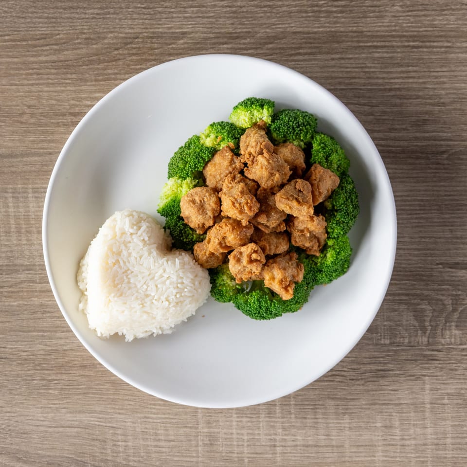 Fried chicken pieces surrounded by broccoli florets, with a heart-shaped mound of white rice.