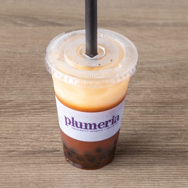 Plumeria Thai iced tea with boba and a black straw, on a wooden table.