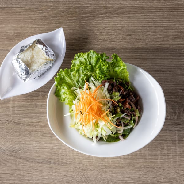 A white bowl of beef salad with lettuce, shredded carrots, and cabbage, next to sticky rice.