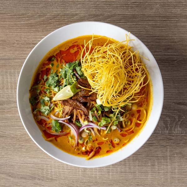 Top-down view of a bowl of Khao Soi, a Thai curry noodle soup, on a wooden table.