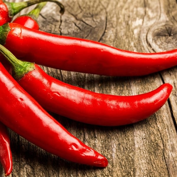 Bright red chili peppers with green stems rest on a rustic wooden surface.