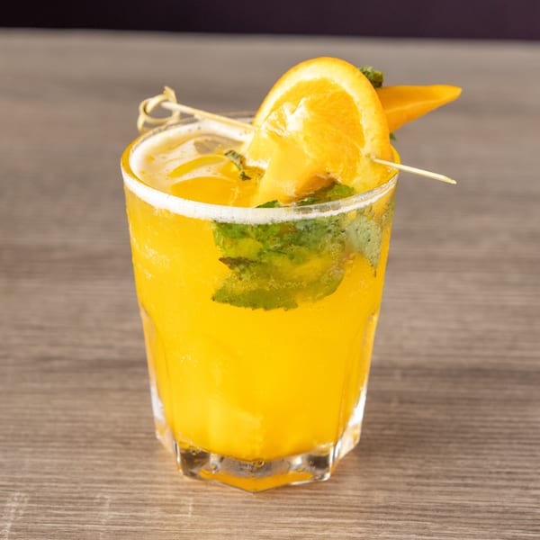 A vibrant orange cocktail with mint leaves and an orange slice garnish on a wooden table.